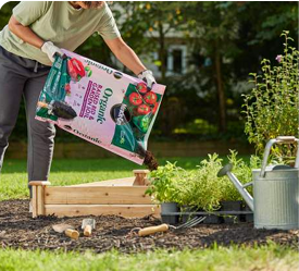 A person pouring soil from a bag into a raised garden bed outside.