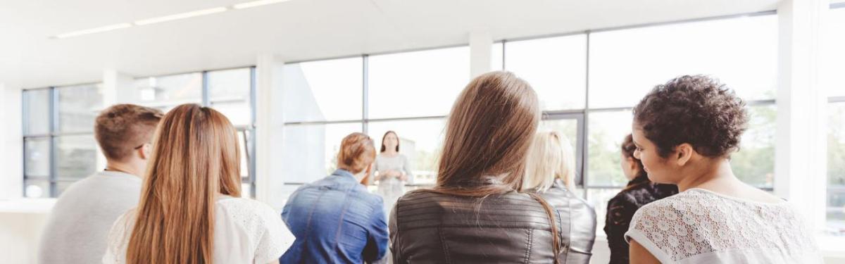 People sitting in a classroom in front of large, sunny windows