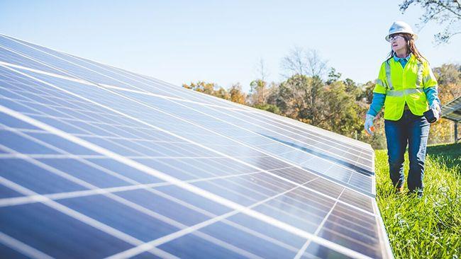 worker in safety gear inspects solar panels installed on a grassy field