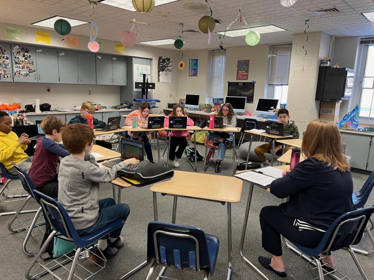 Karen Braun and students at desks in a circle in a classroom.