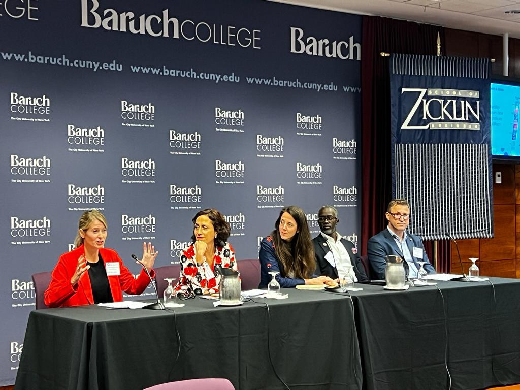 A panel of five people at the front of a room, one speaking.