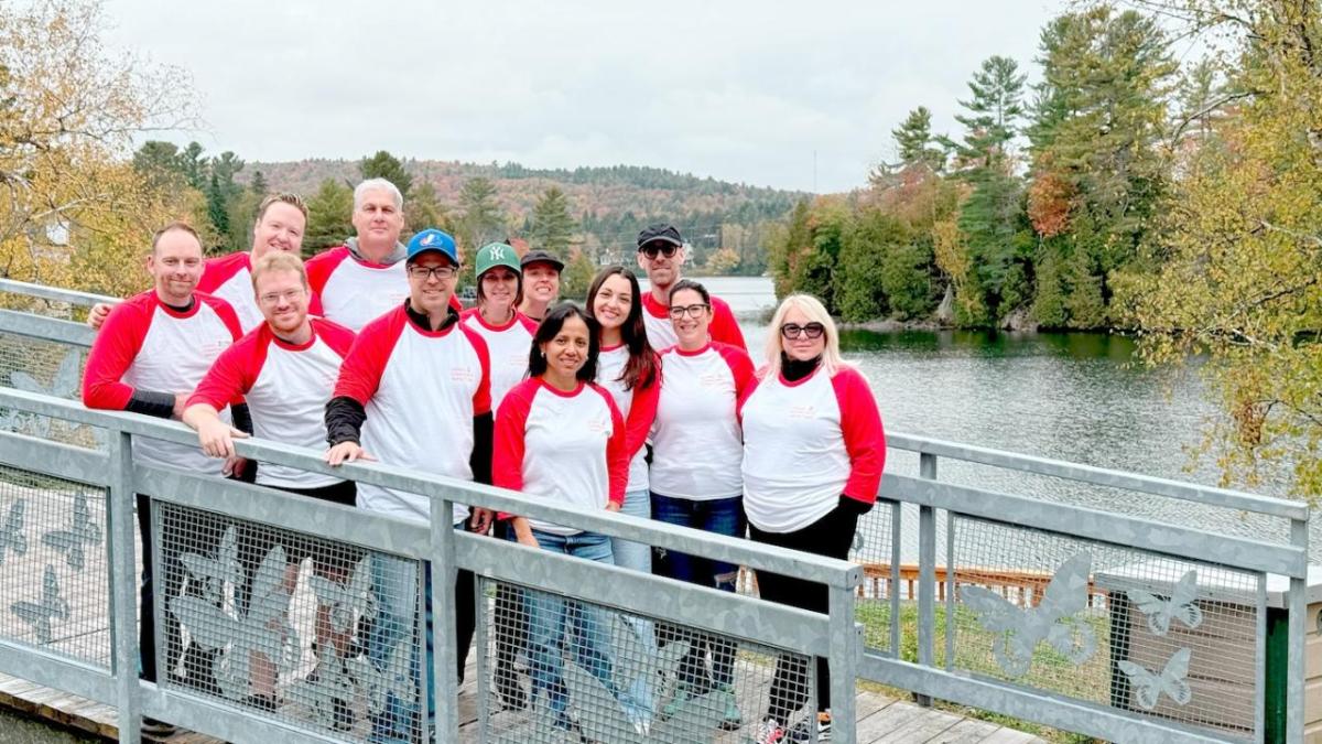 A group of people stood together on a bridge wearing matching white and red long sleeve tops