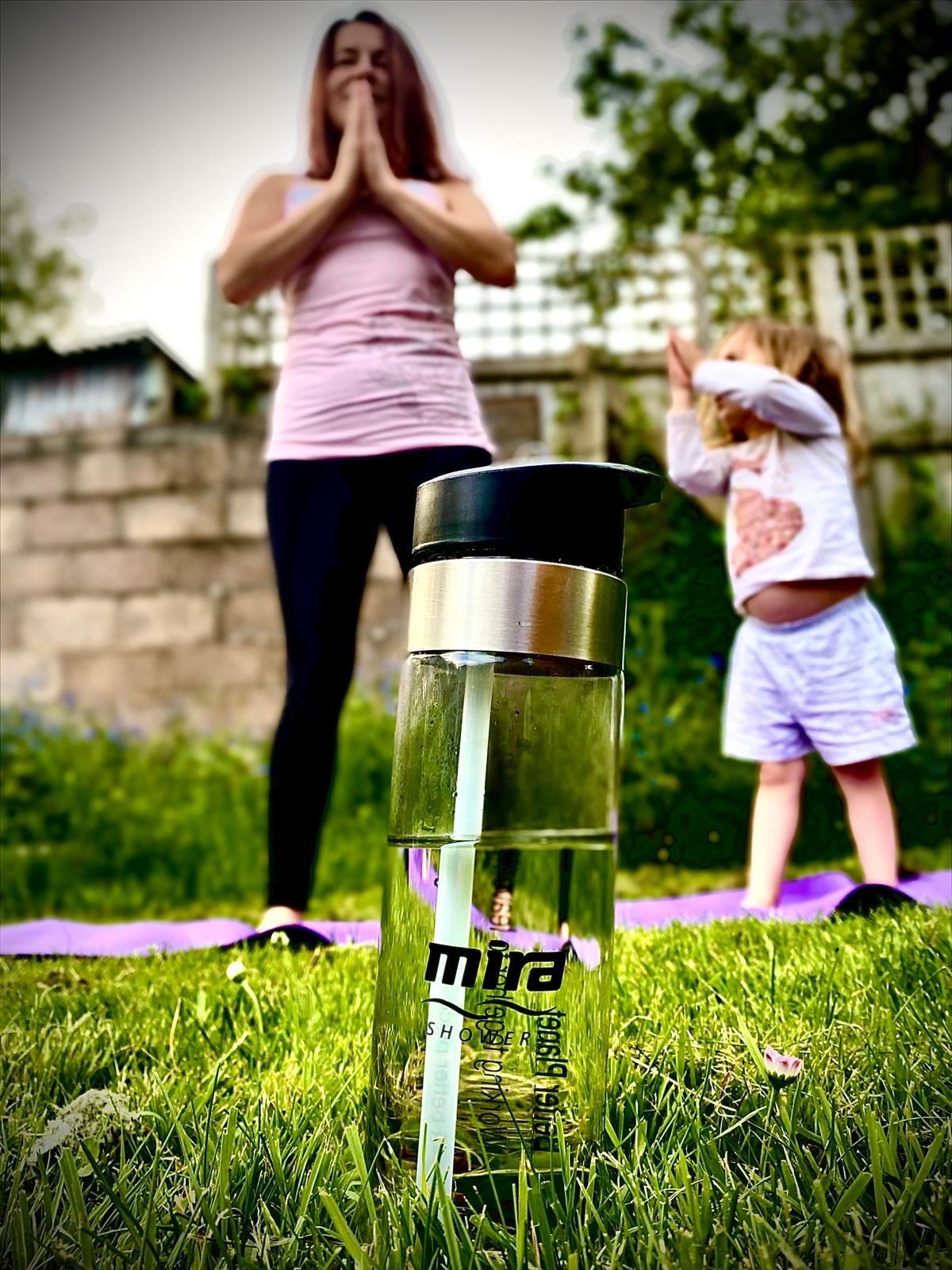 An adult and child doing stretches in a park setting.