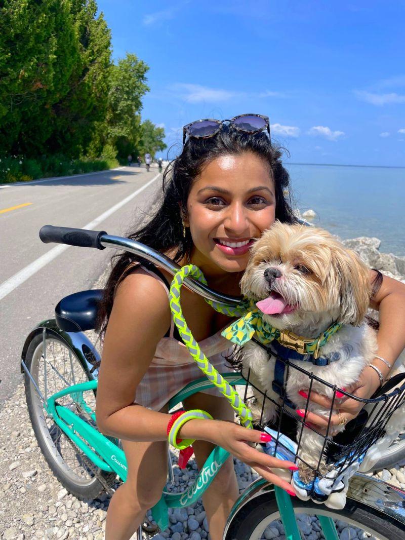 A person biking outside with a small dog in a front basket.