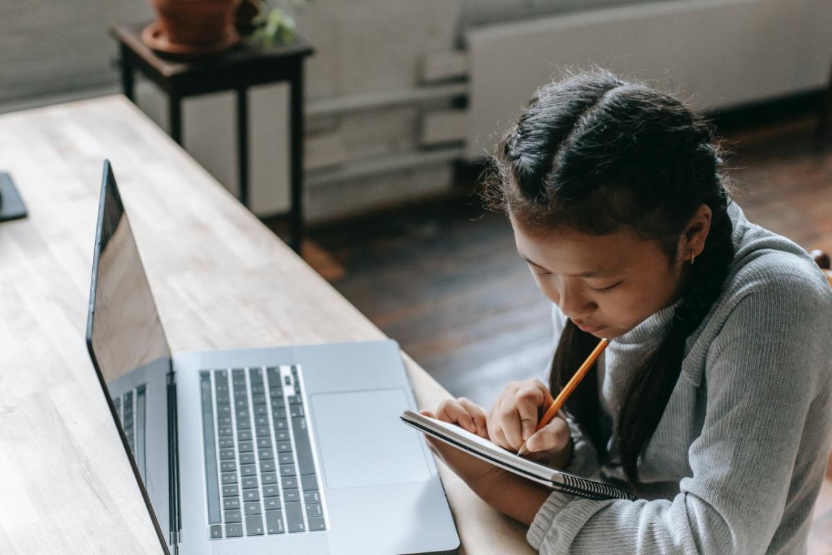 girl with laptop writing in notebook