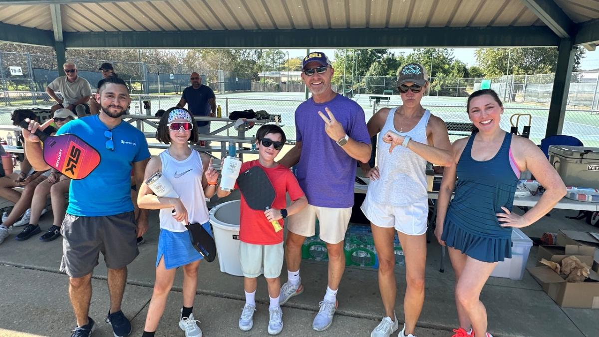 A group posed under a roof, some with pickleball equipment