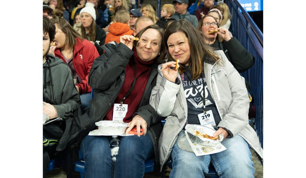 Two people in the crowd eating pizza