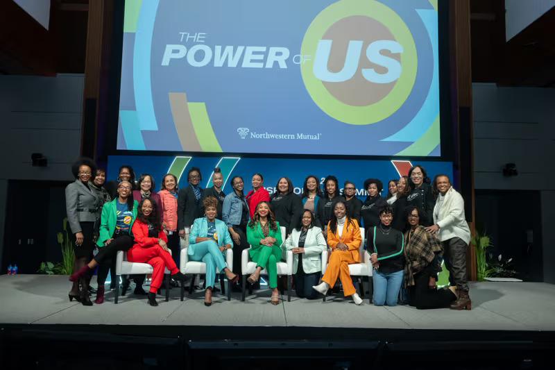 A group posed on a stage. "The Power of Us" displayed behind them.