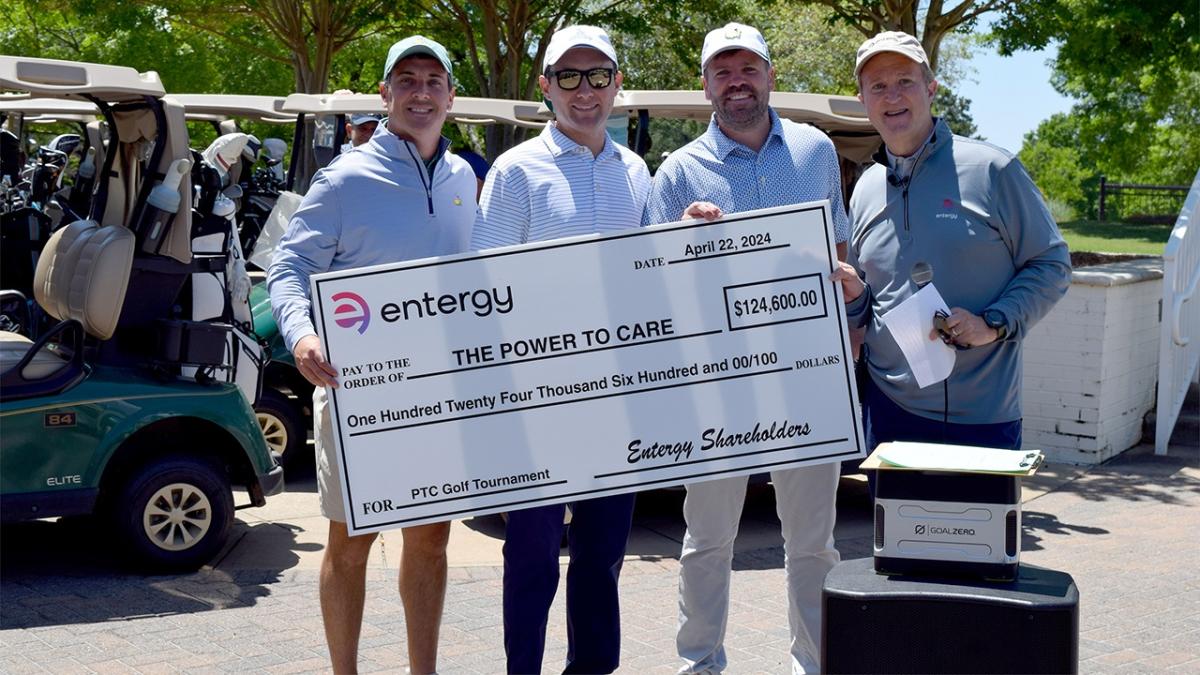 Four people posed with a large check. Golf carts to the side.