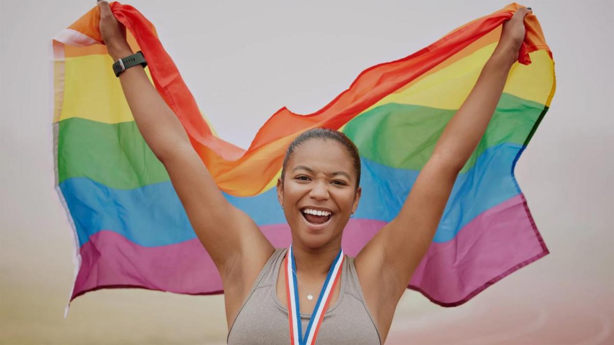 An athlete holding a rainbow flag behind them.