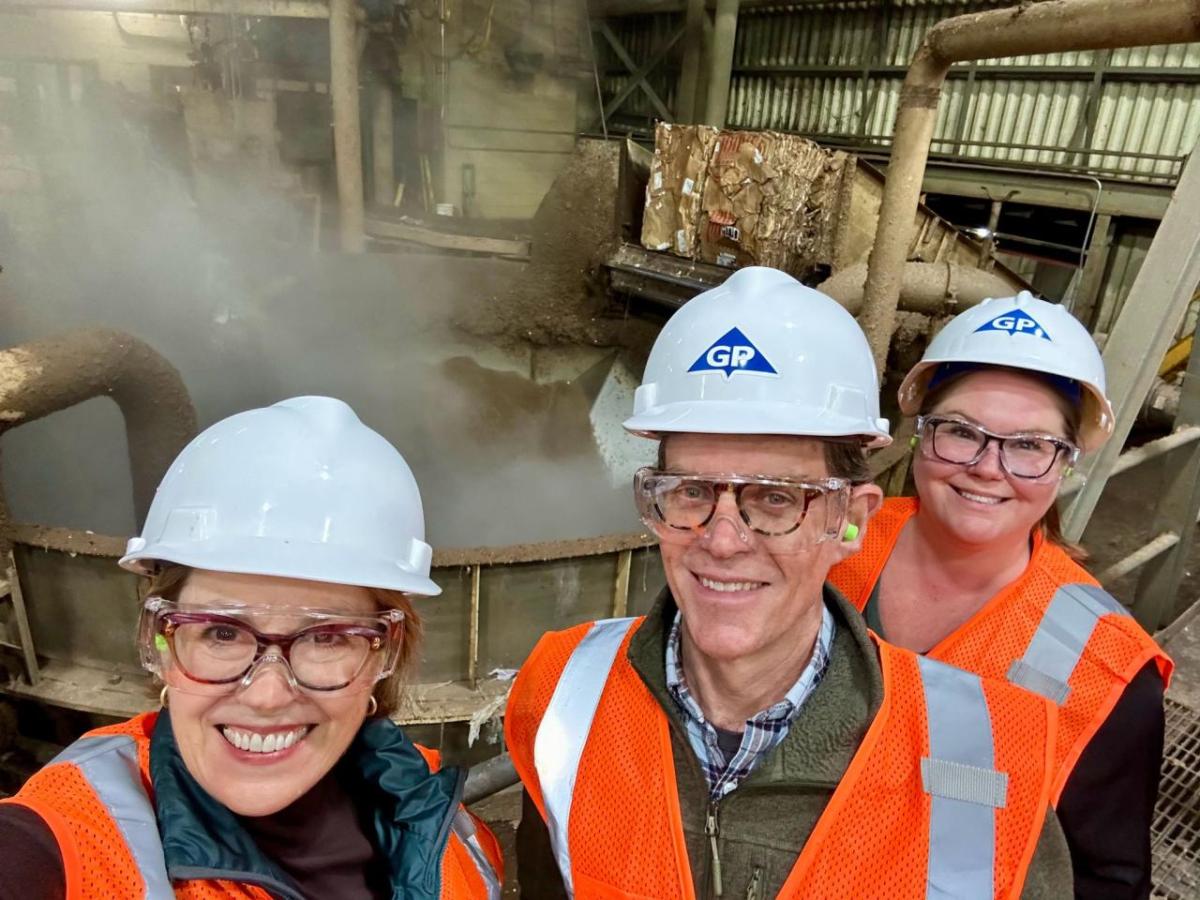 Three people smiling in front of a steaming machinery