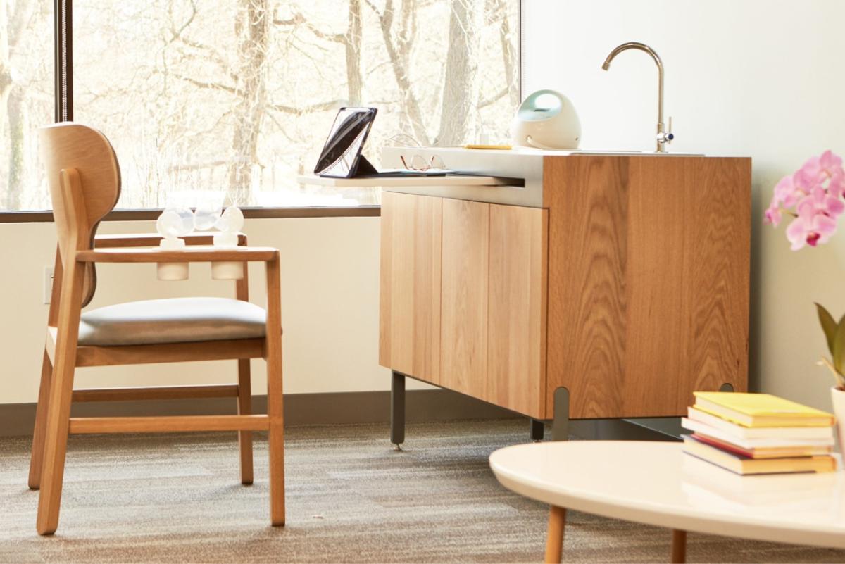 a room with a large window, specialized nursing chair, sink and coffee table.