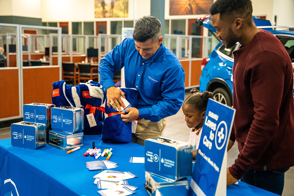 Two adults and a child at a "Subaru Loves to Care" table