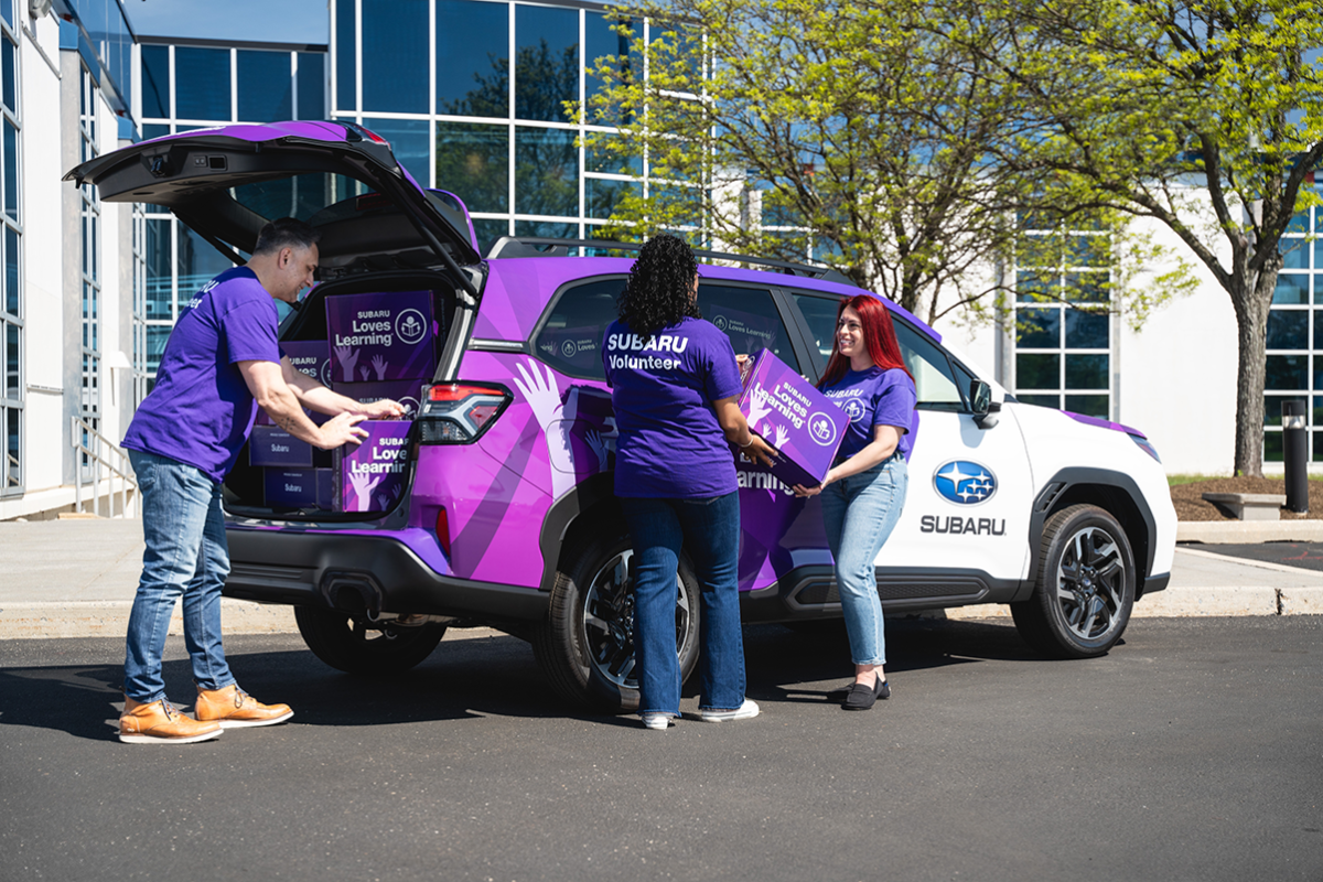 Three people putting boxes into a purple Subaru vehicle