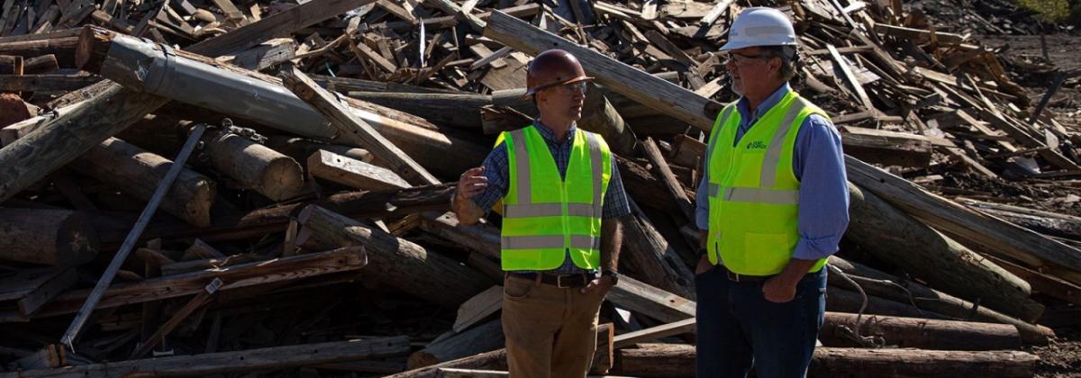 2 workers standing in front of a pile of old power poles