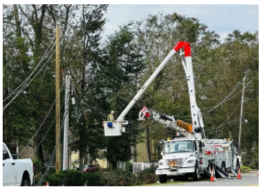 A bucket truck with worker in the lift next to power lines.