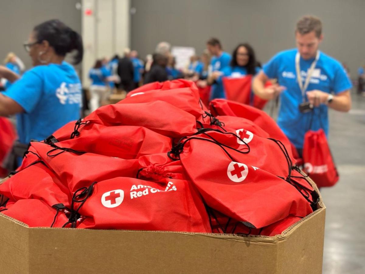 A box filled with American Red Cross bags. Volunteers in the background.