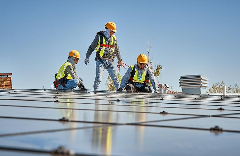 Three people in high-vis garments and hard hats installing solar panels.