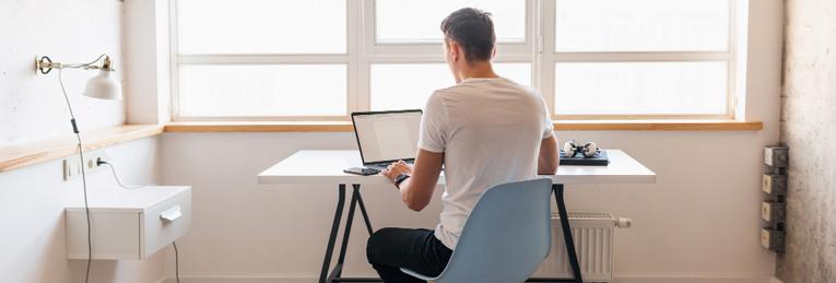 Person sitting at a desk with a laptop, in front of a bright window