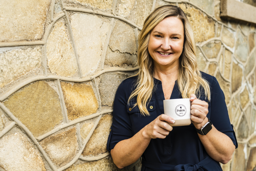 A person holding up a coffee mug next to a tan stone wall.