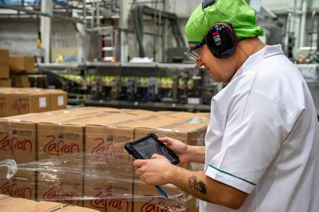 A person with ear protection using a tablet in a warehouse setting.