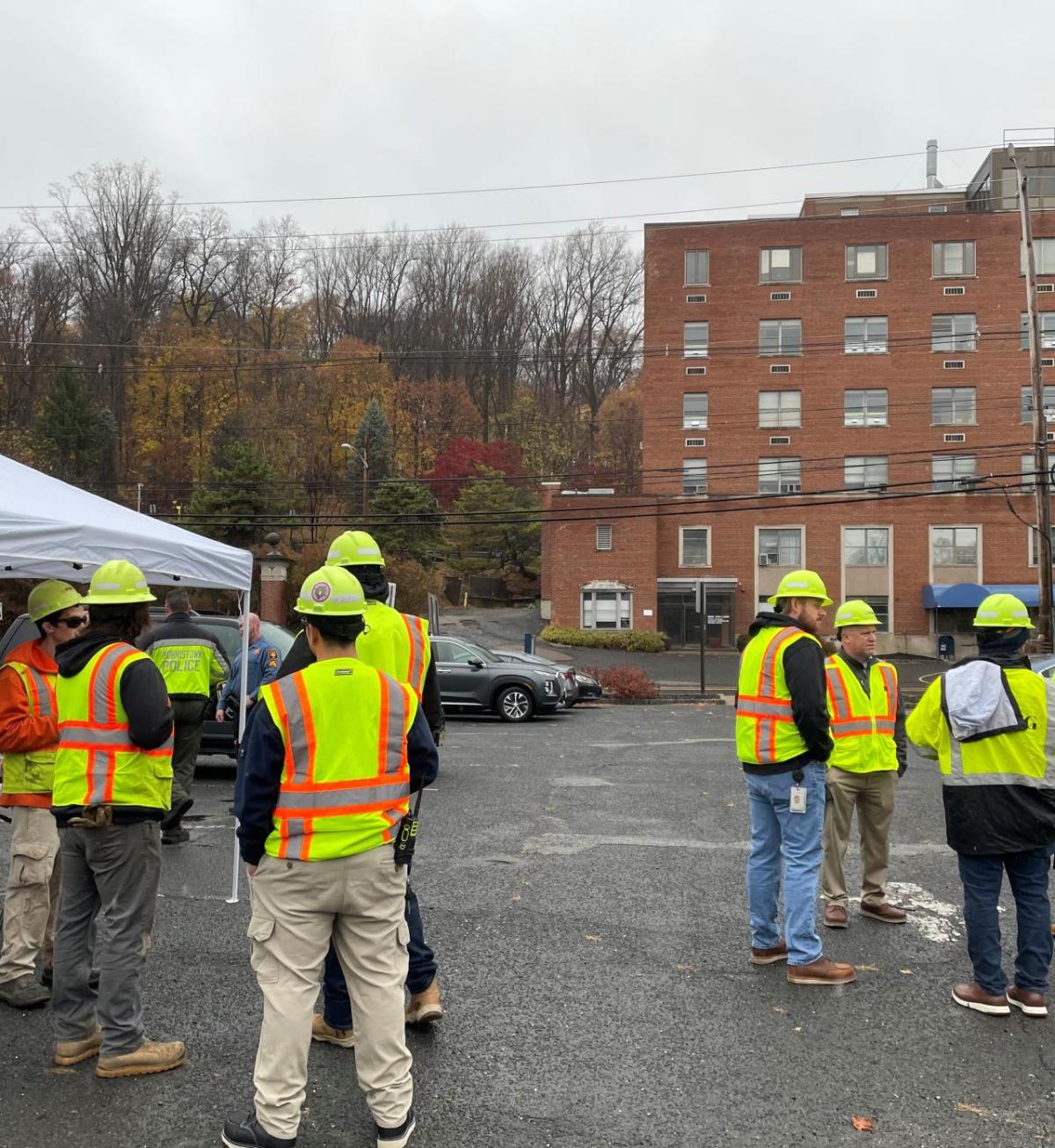 Employees standing outdise in a parking lot wearing high vis vests and hard hats.