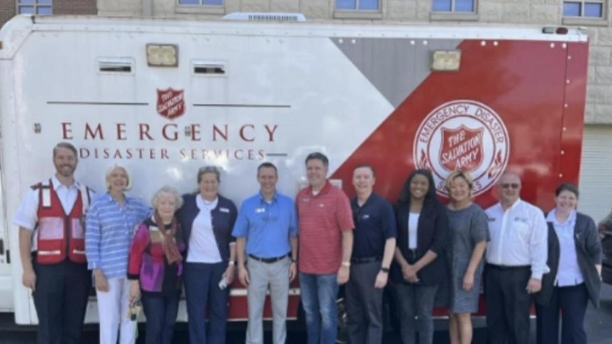 A row of people posed in front of a trailer with salvation army signs.