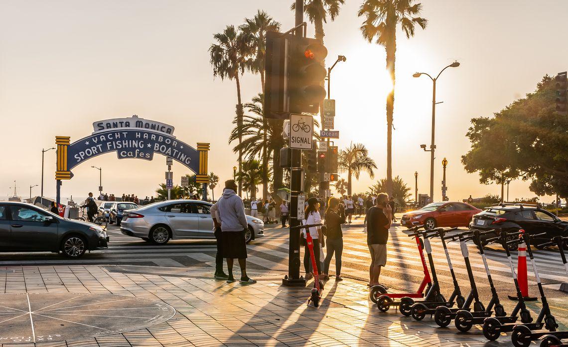 sunset over santa monica yacht harbor. Traffic and pedestrians and a row of rentable scooters