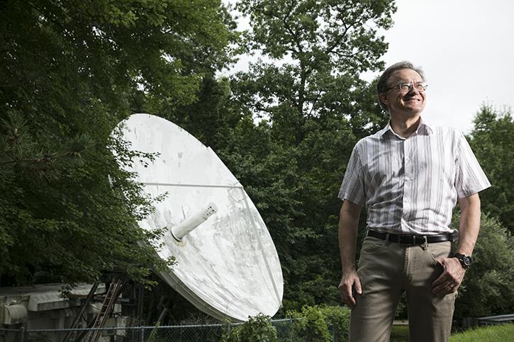 A person standing outside looking to the sky, a large satellite dish behind them