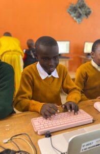 A smiling child using a computer next to others.