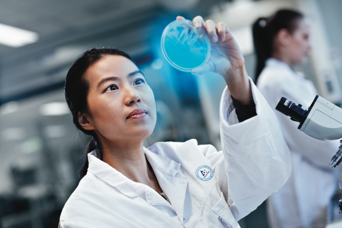 A person in a lab jacket holding up a petri dish that's glowing blue