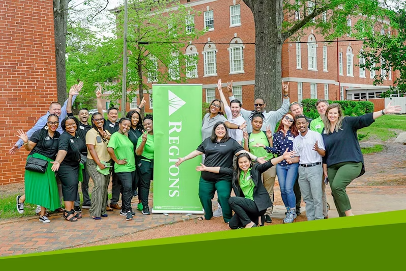 A group of people posing outside next to a Regions banner