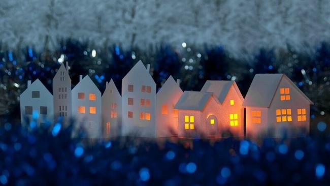 Paper cutout houses with warm light shining within, and tinsel surrounding them