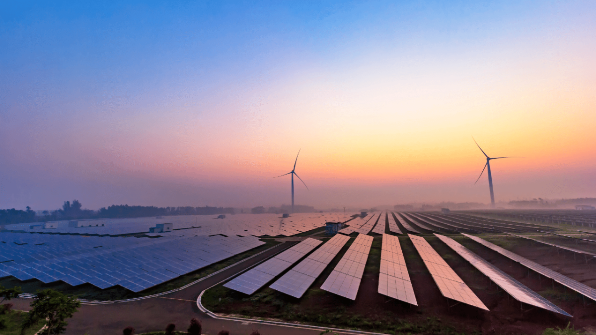 Foggy sunrise over a field of solar panels. Wind turbines in the distance.