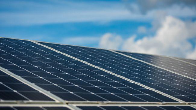 Close up of a solar panel, a blue partly cloudy sky behind.