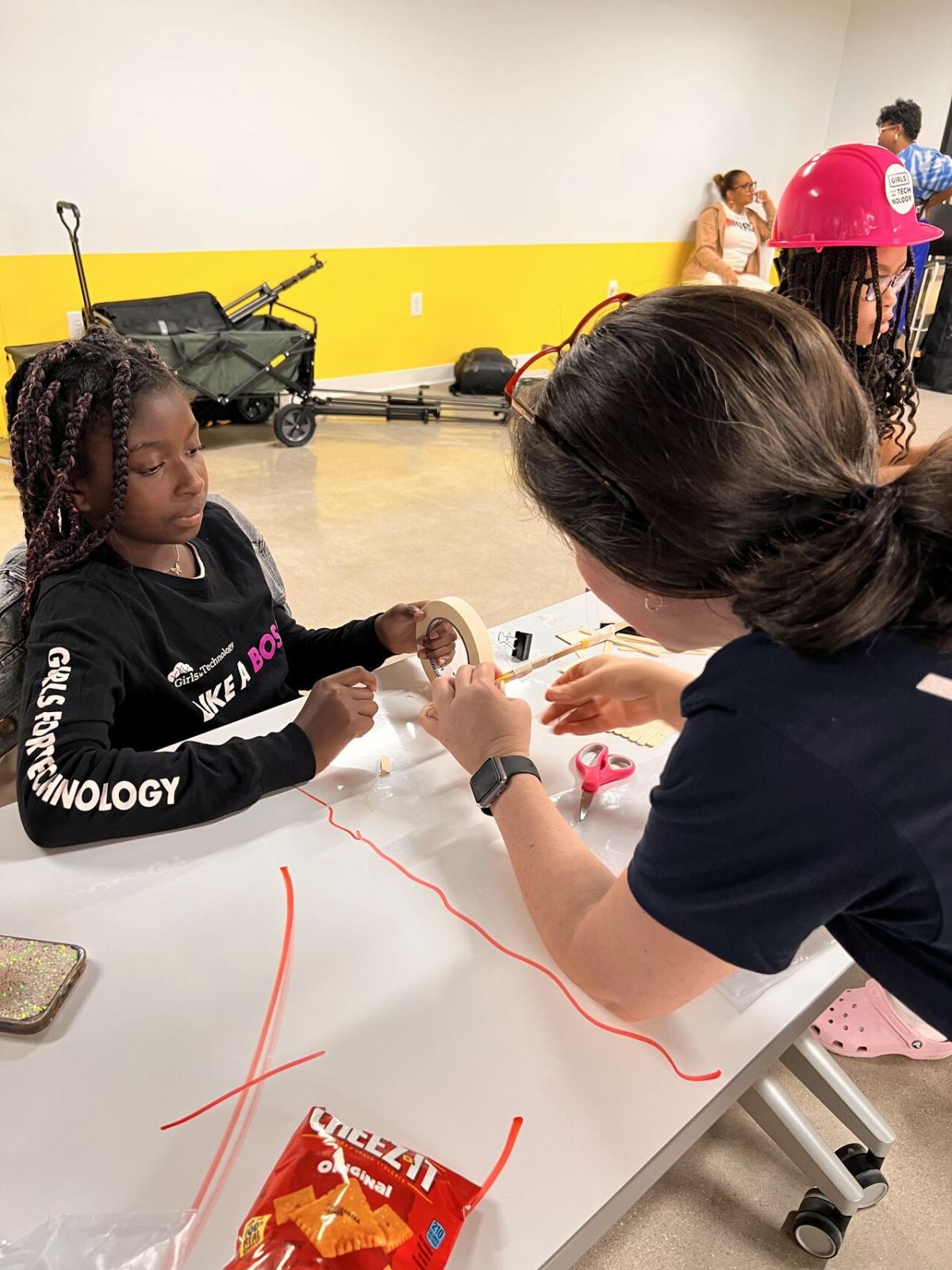 Adult volunteers and children working on building model structures with craft supplies.