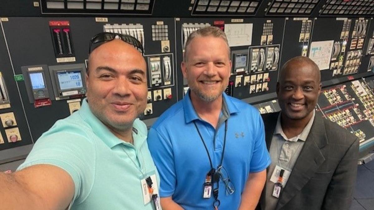 Three people posed for a selfie in front of a wall of controls.