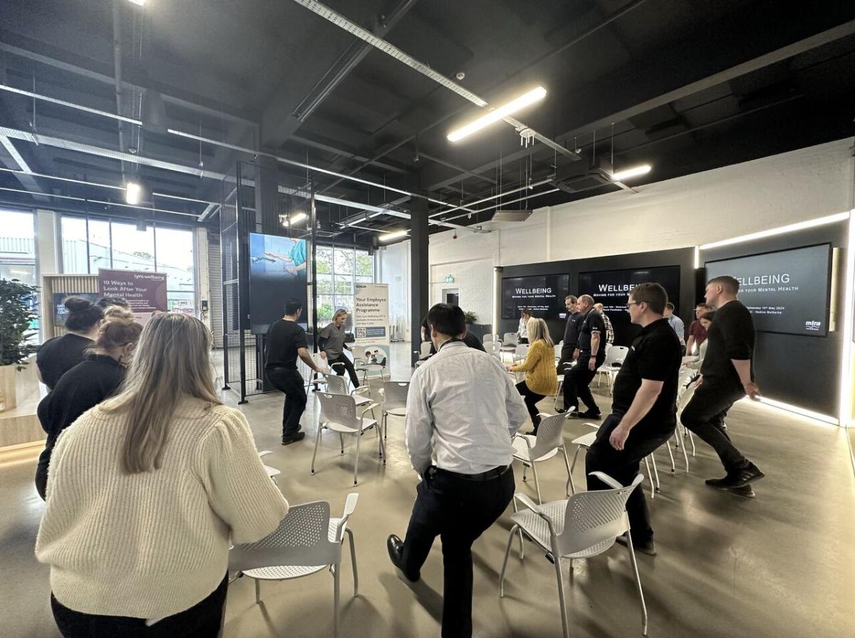 A group in a circle standing next to their chairs doing stretches.