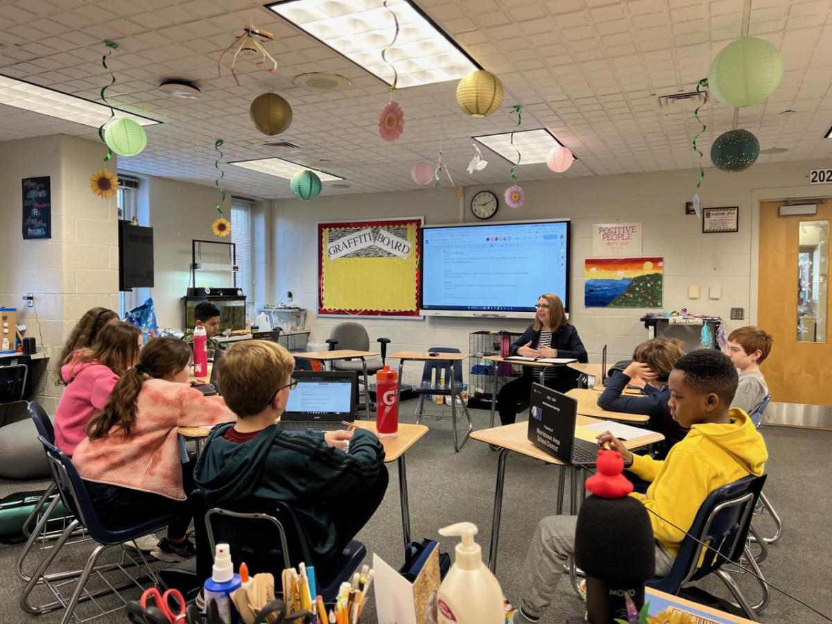 Karen Braun and students at desks in a circle in a classroom.