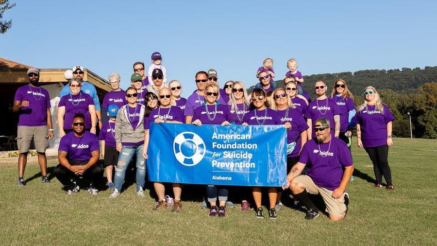 A group of people in matching shirts outdoors. Some holding a sign "American Foundation for Suicide Prevention."