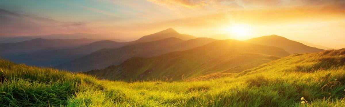 A sunset over mountain range with grassy plains.