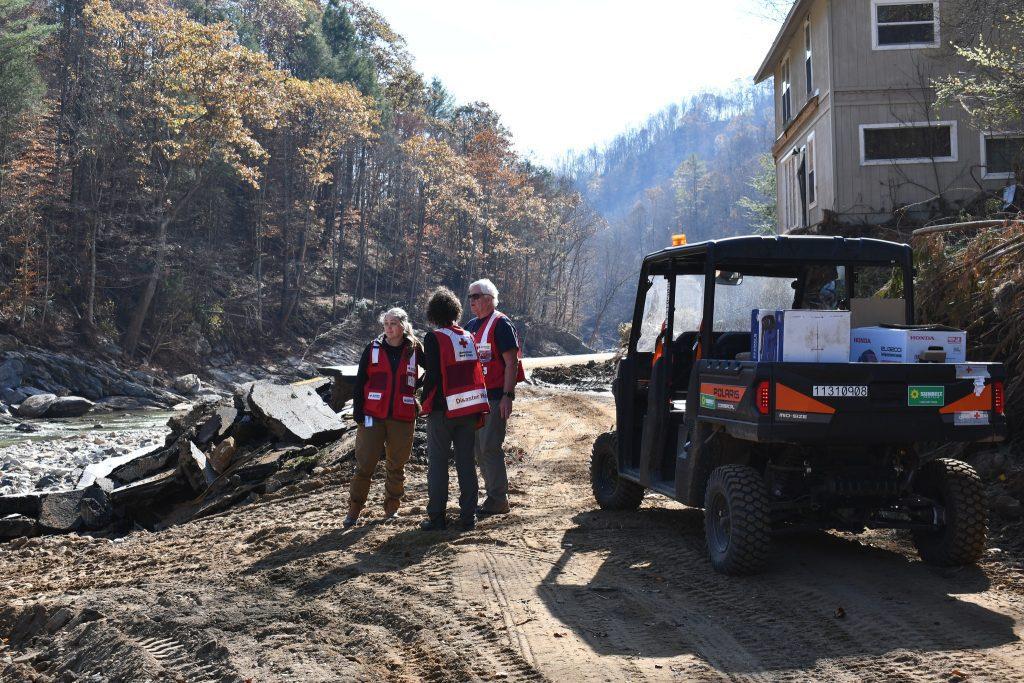 Three workers talking together next to a river, and a vehicle loaded with supplies