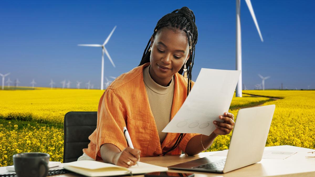 Person taking notes at a desk that is in a field with wind turbines.