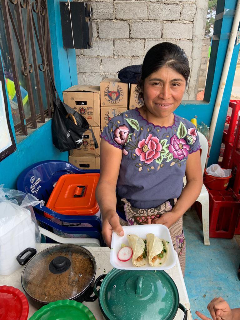 A person handing the photographer a plate of food.