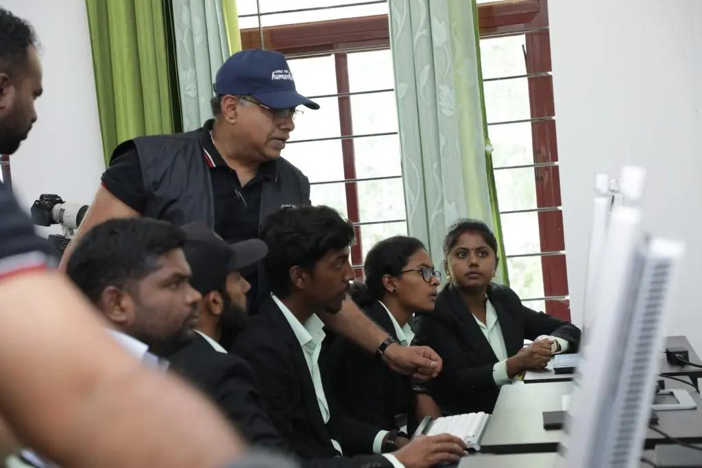 An adult looking over students using computers.