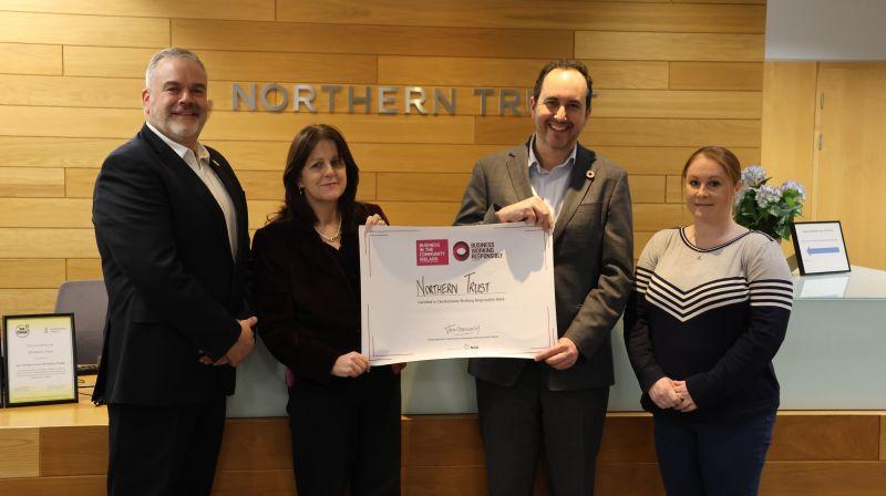 Four people in a lobby "Northern Trust" on the wall behind them. Two holding a plaque.