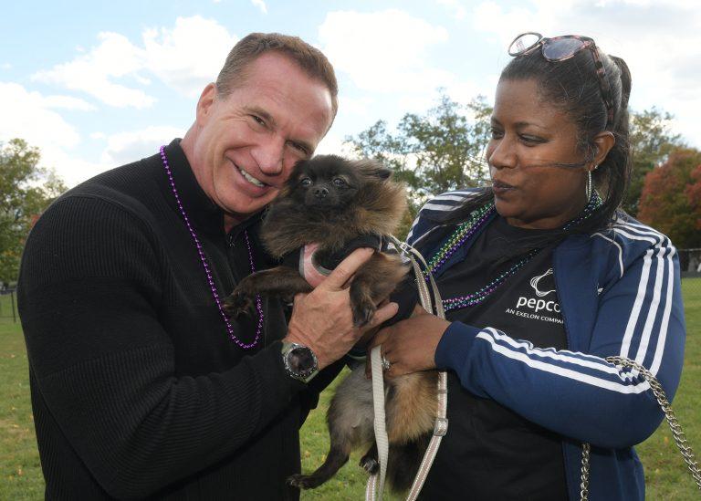 Two people holding a small dog between them outside.