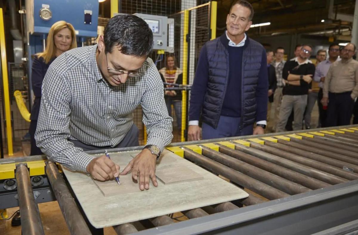 Matthew Sanchez signing the back of a tile on a conveyor line.