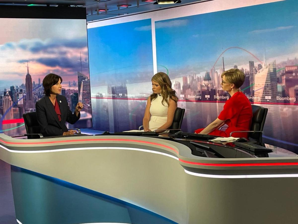 Tracey and two others seated behind a desk on a set.