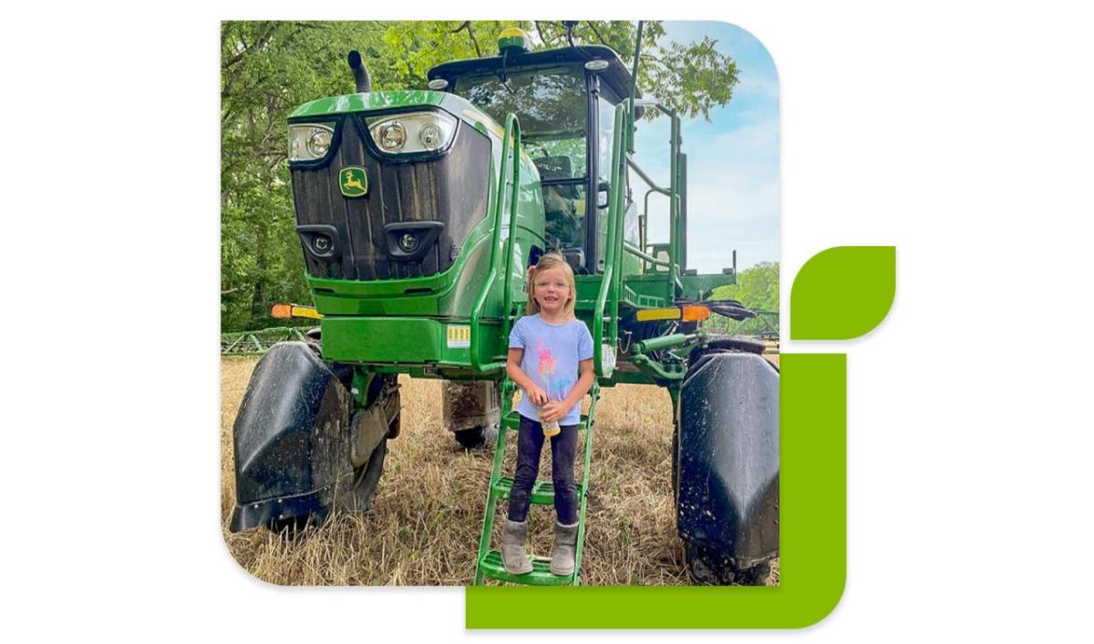 A child on the steps up to a green tractor.